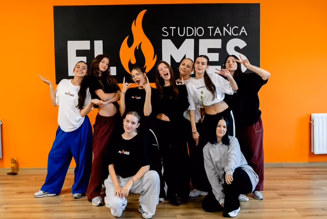 Grupa tancerek pozuje do wspólnego zdjęcia pod logo Studia Tańca Flames